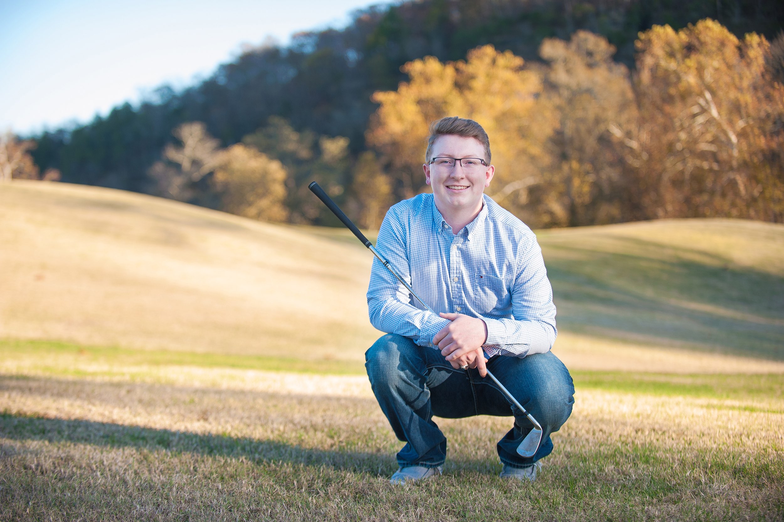 Senior guy in blue shirt and jeans squatting on golf course near Crane, MO.