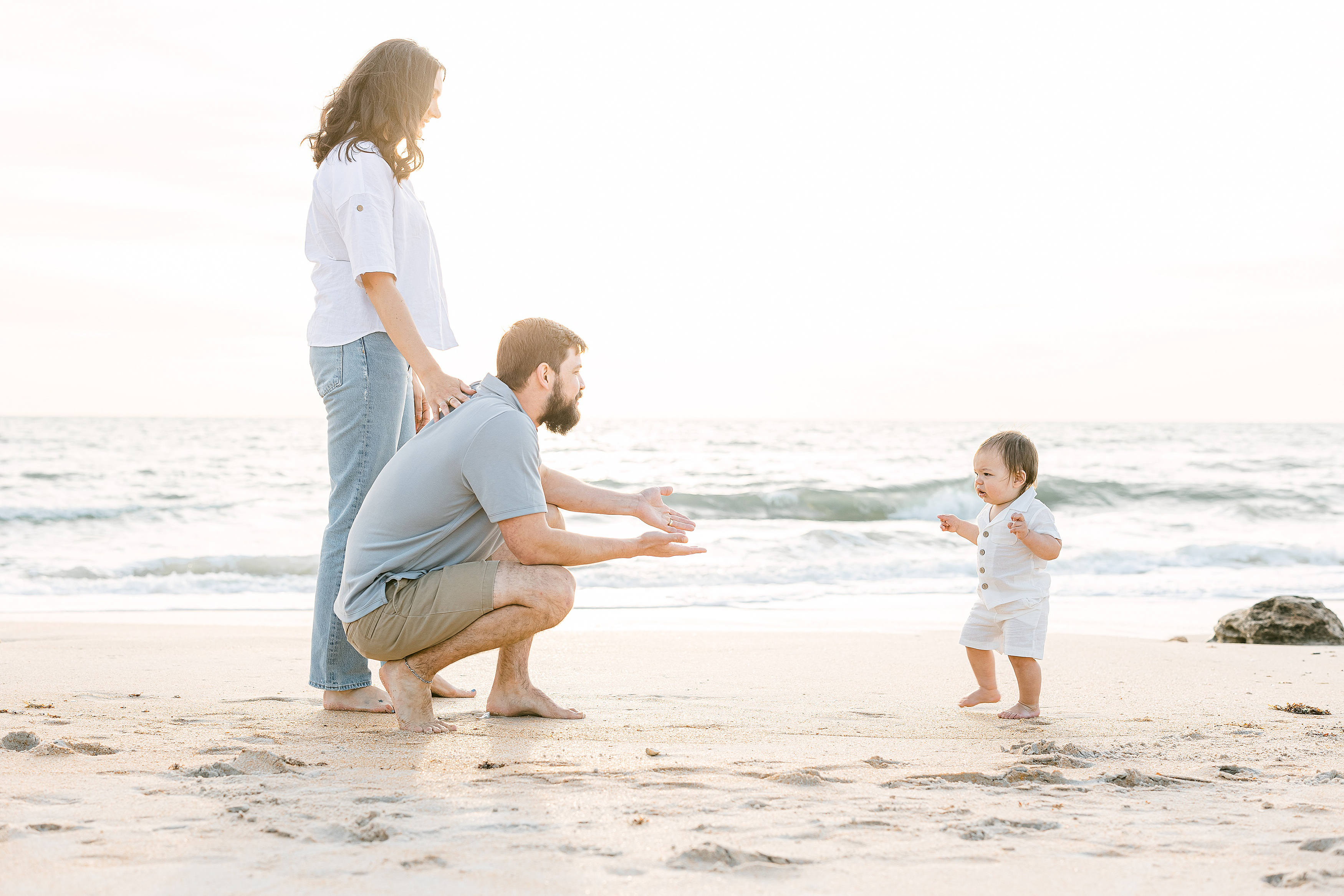 family playing together on the beach at sunrise wearing neutral clothing