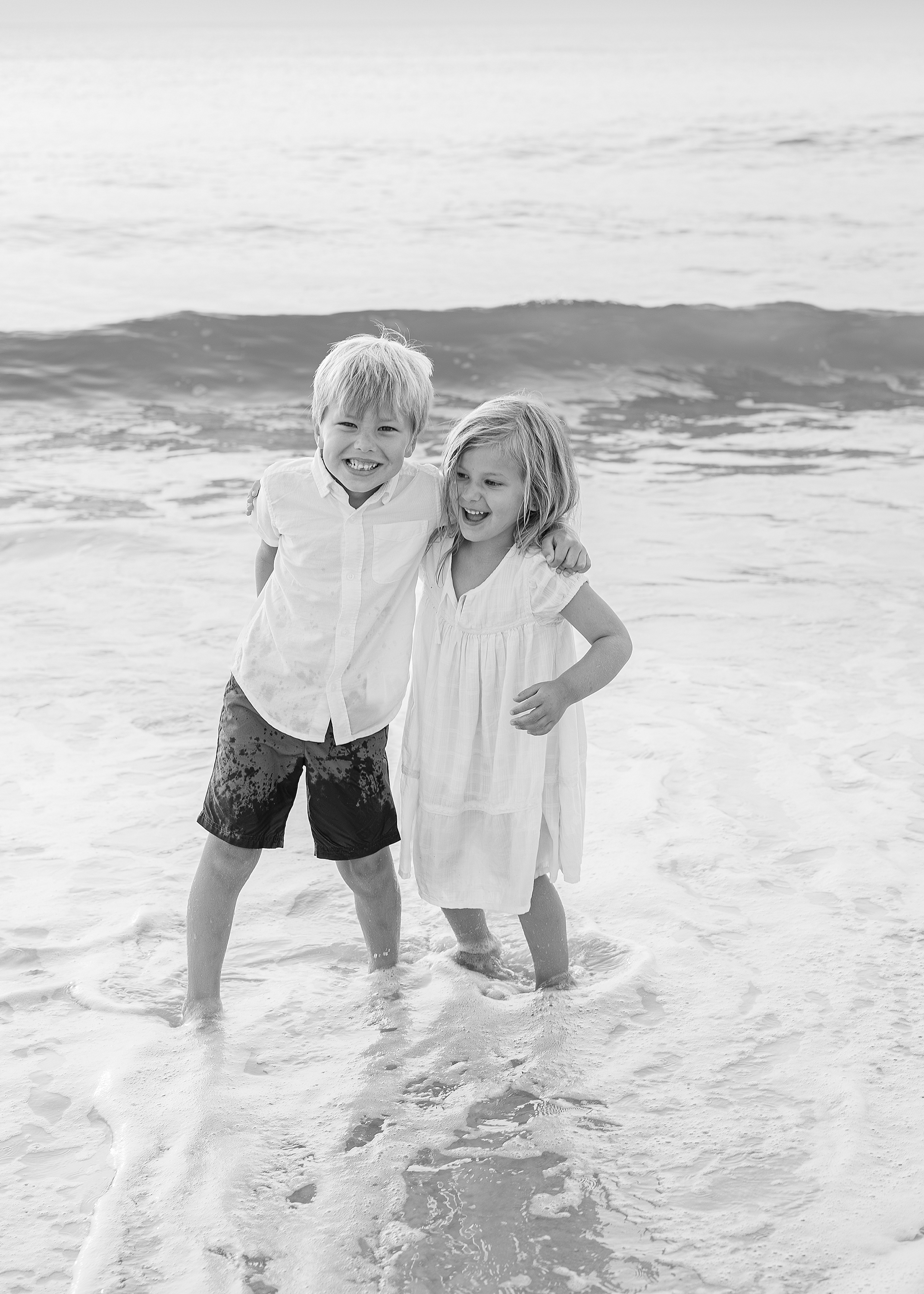 Airy black and white beach portrait of little children playing in the surf together.