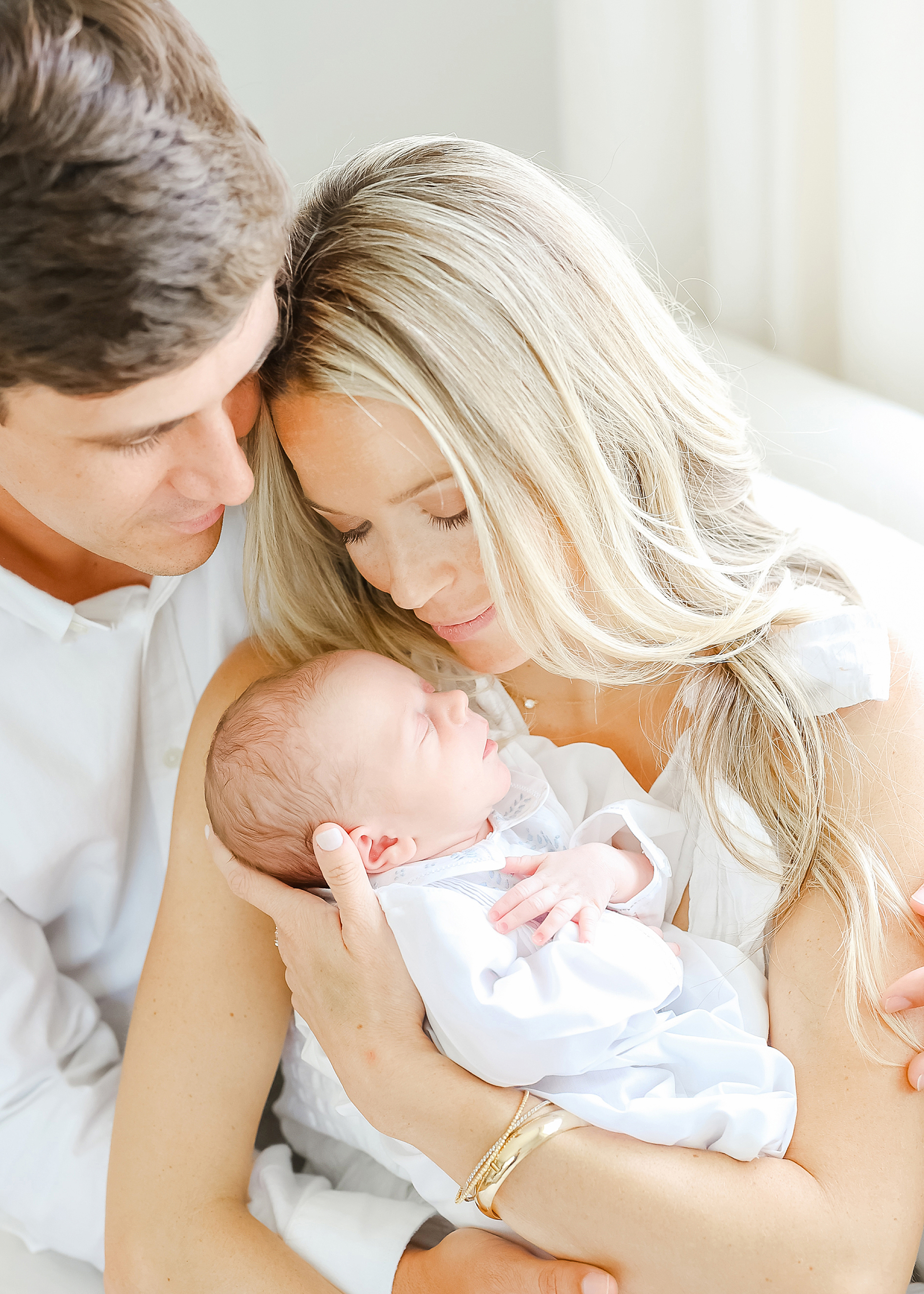 Light and airy newborn portrait of a mother and father holding their newborn son.