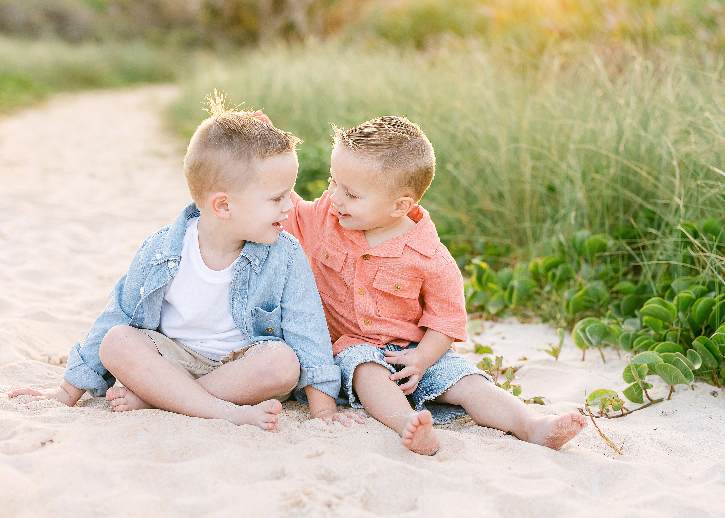 Sun-filled and colorful beach portrait of two little boys sitting on the sand.