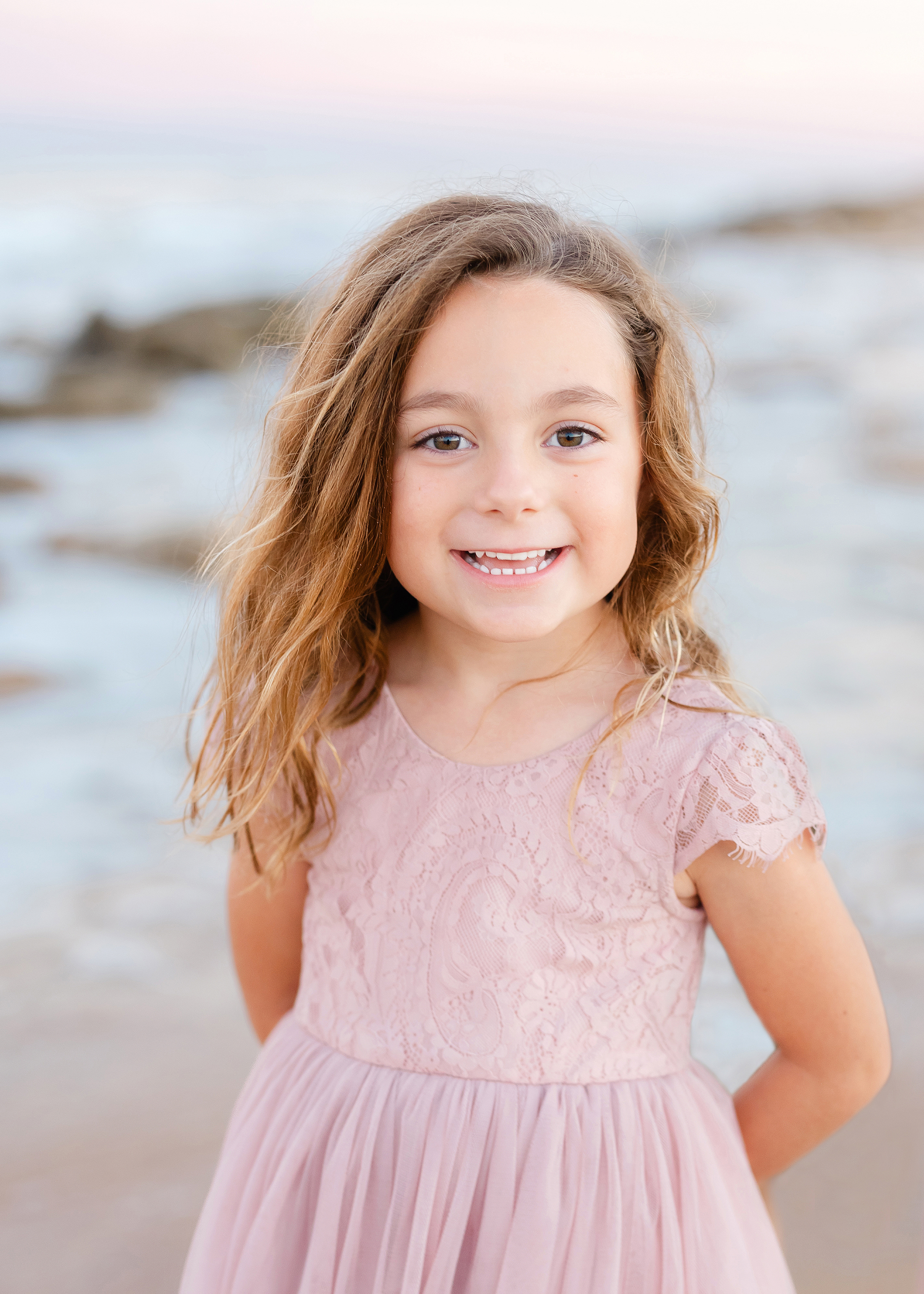 A pastel sunset portrait of a little girl in a pink dress on the beach.