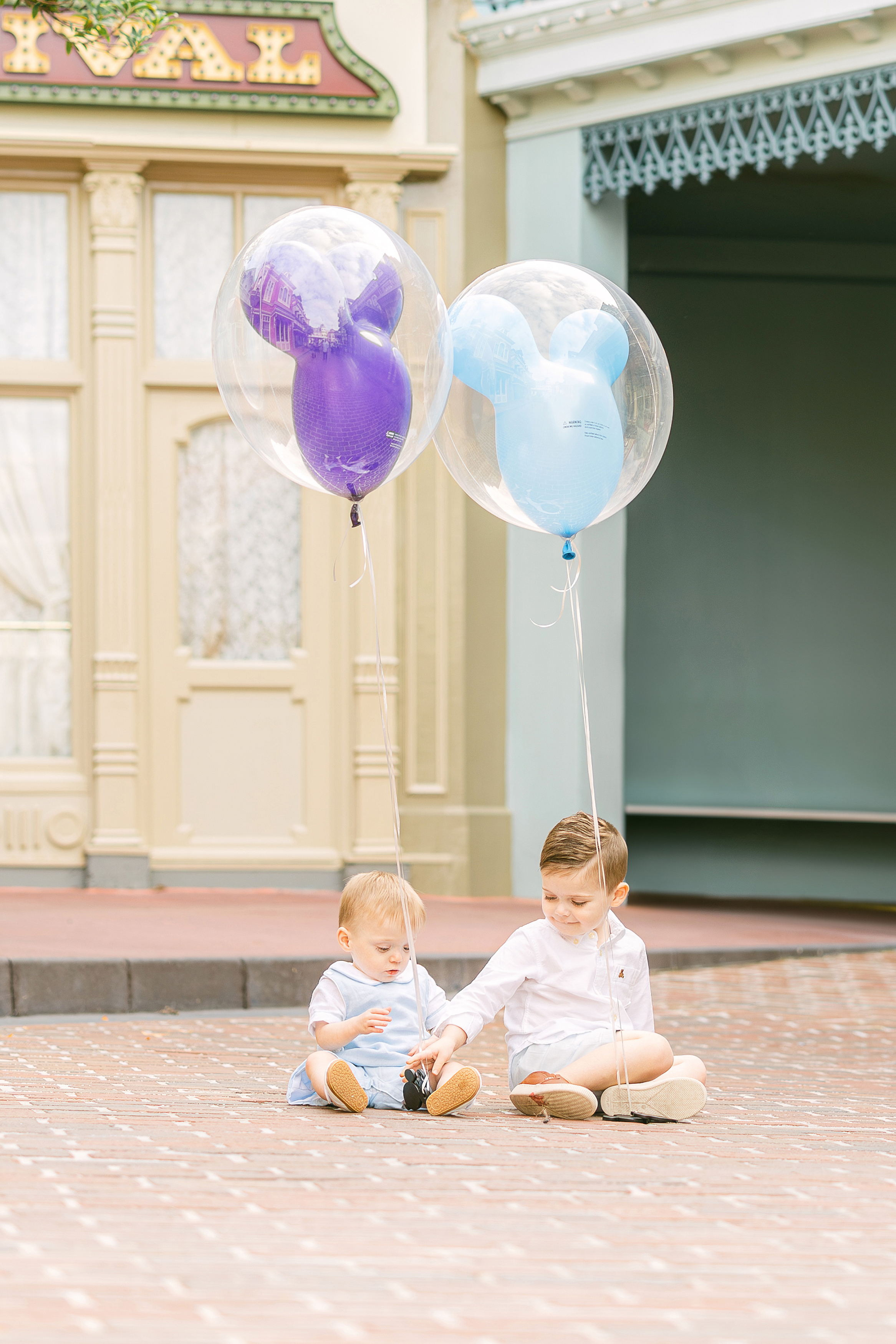 Two little boys holding Mickey Mouse balloons sit on a side street of Main Street U.S.A.