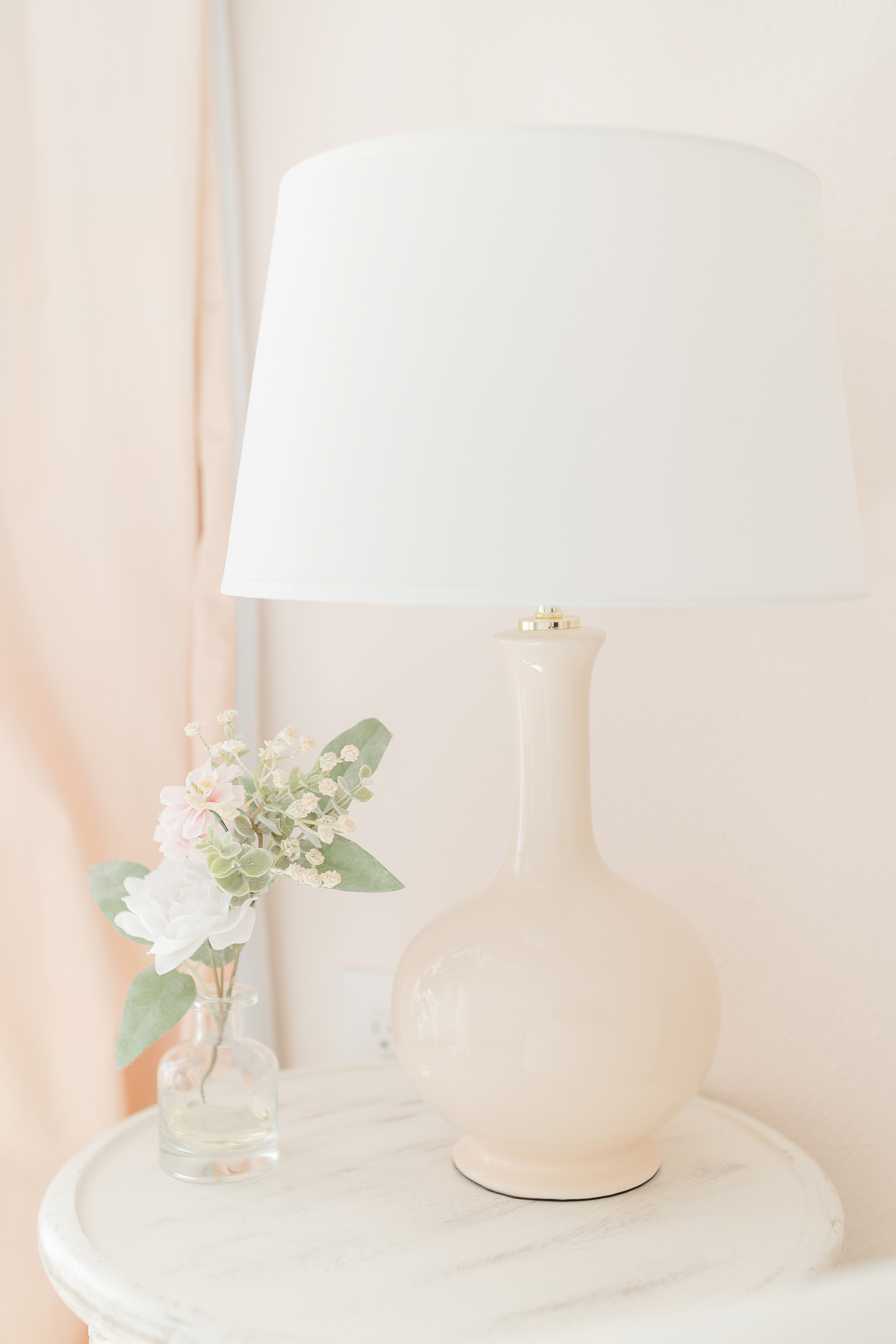 A pink detail nursery image of a lamp and side table in a newborn baby girl room.