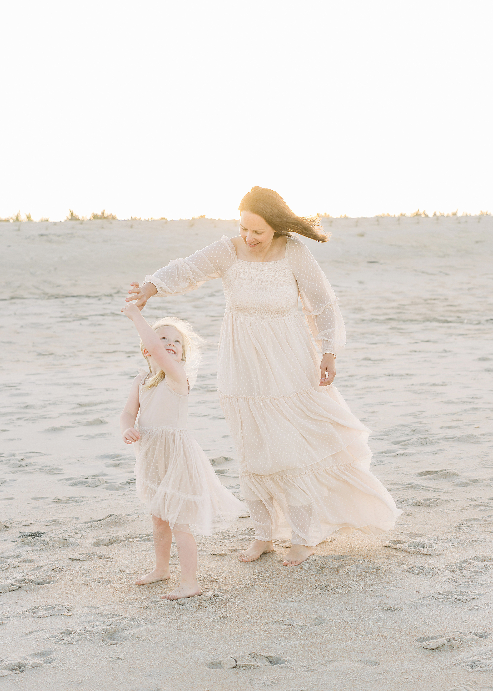 A woman twirls her little girl on the beach at sunset.