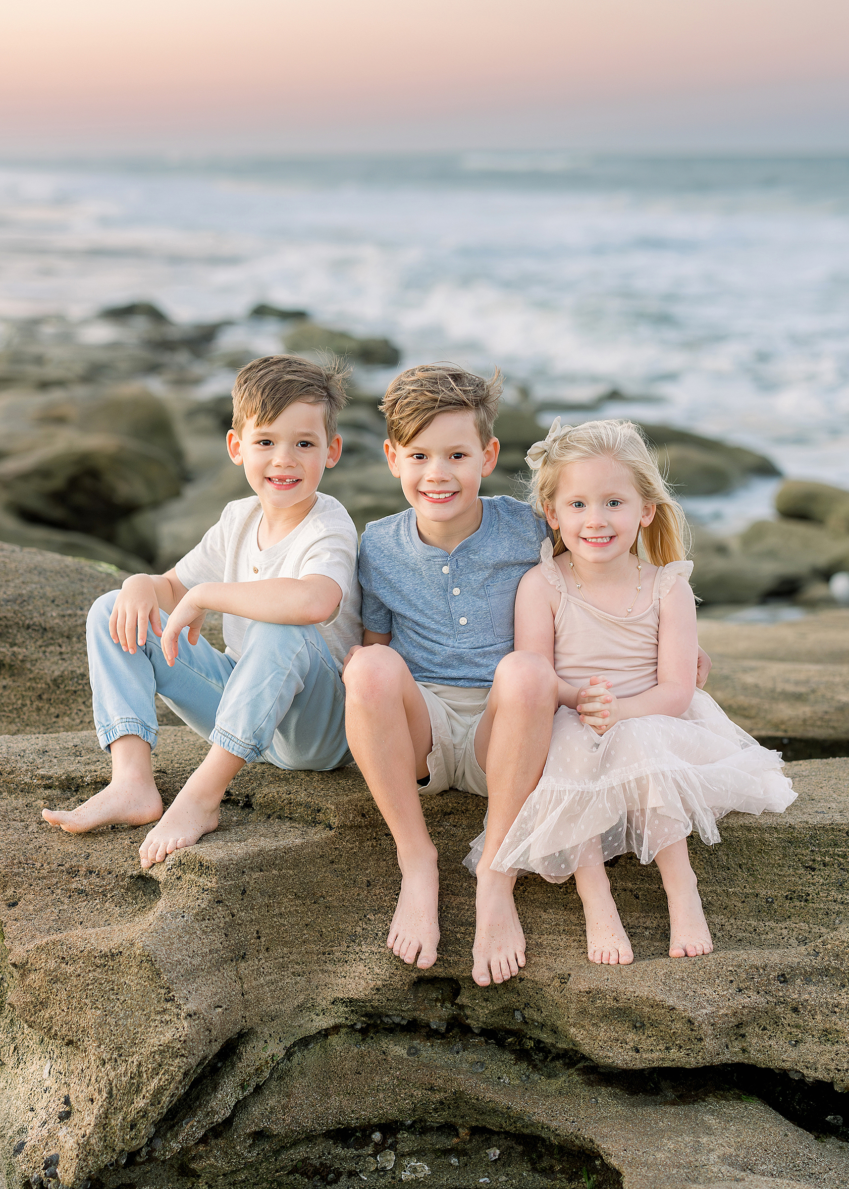 A family of five sit together on the beach at sunset.