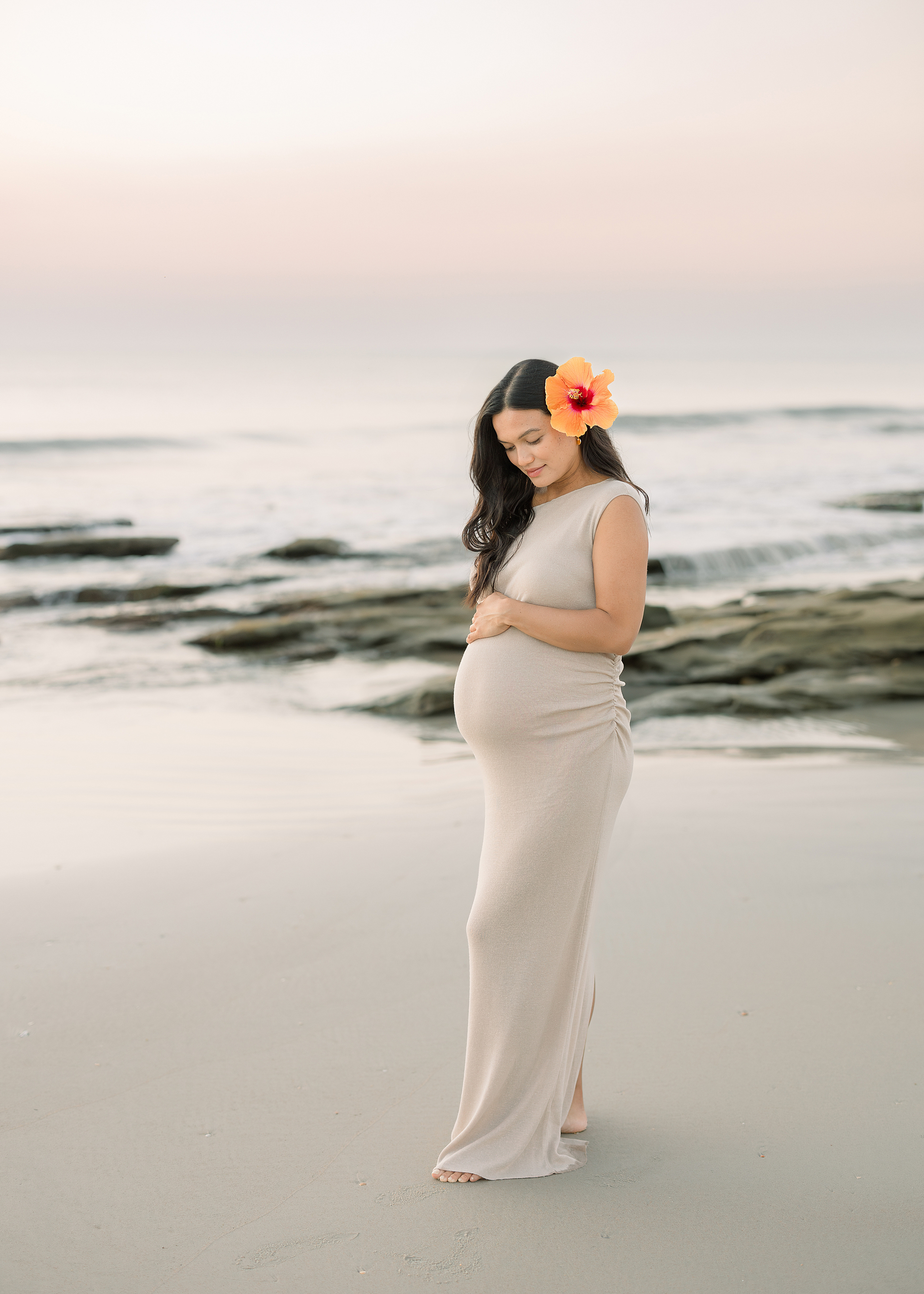 A sunrise pregnancy portrait of a woman with black hair and a flower in her hair on St. Augustine Beach.