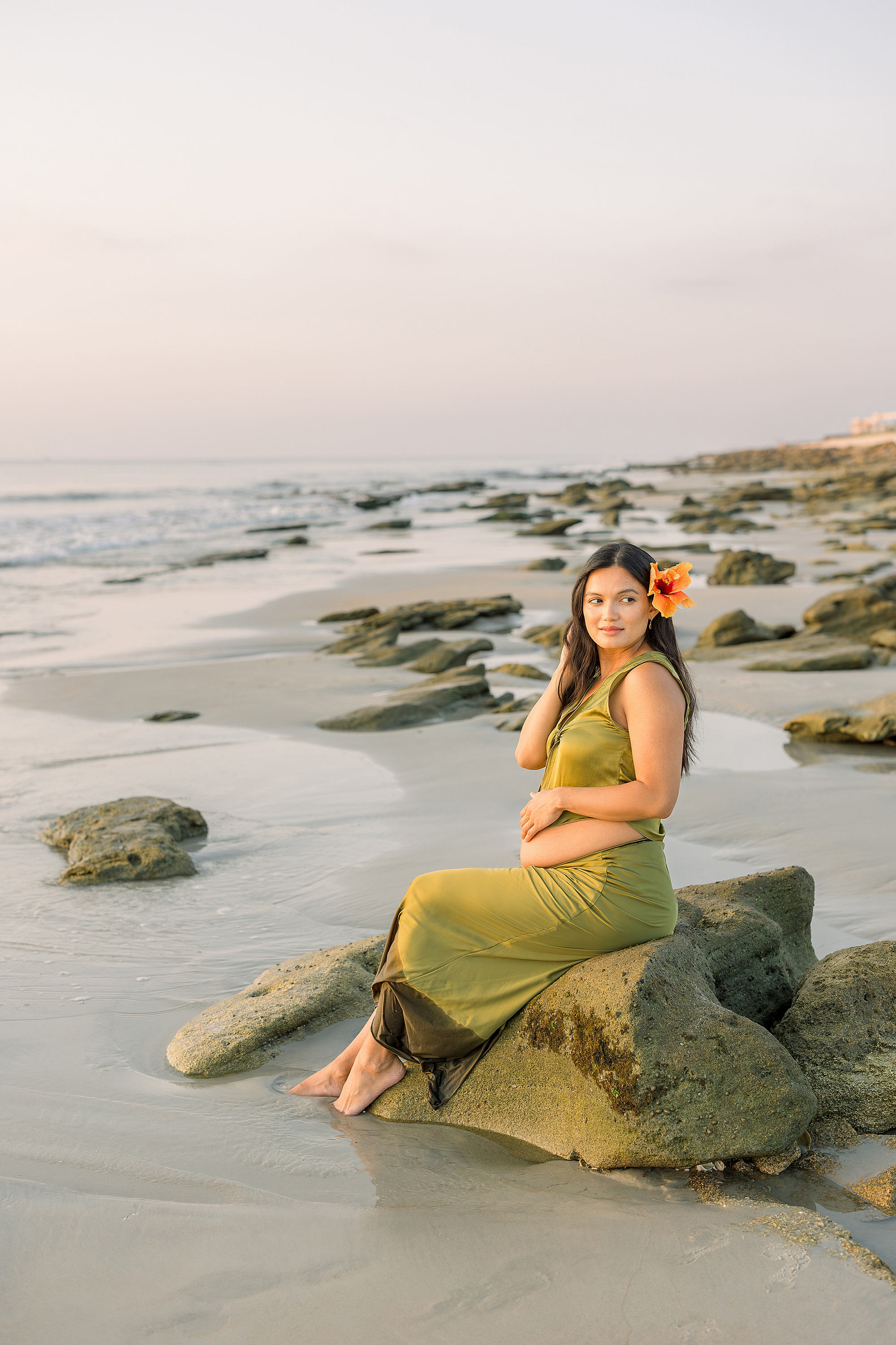 A woman with dark hair in green satin on the beach at sunrise.