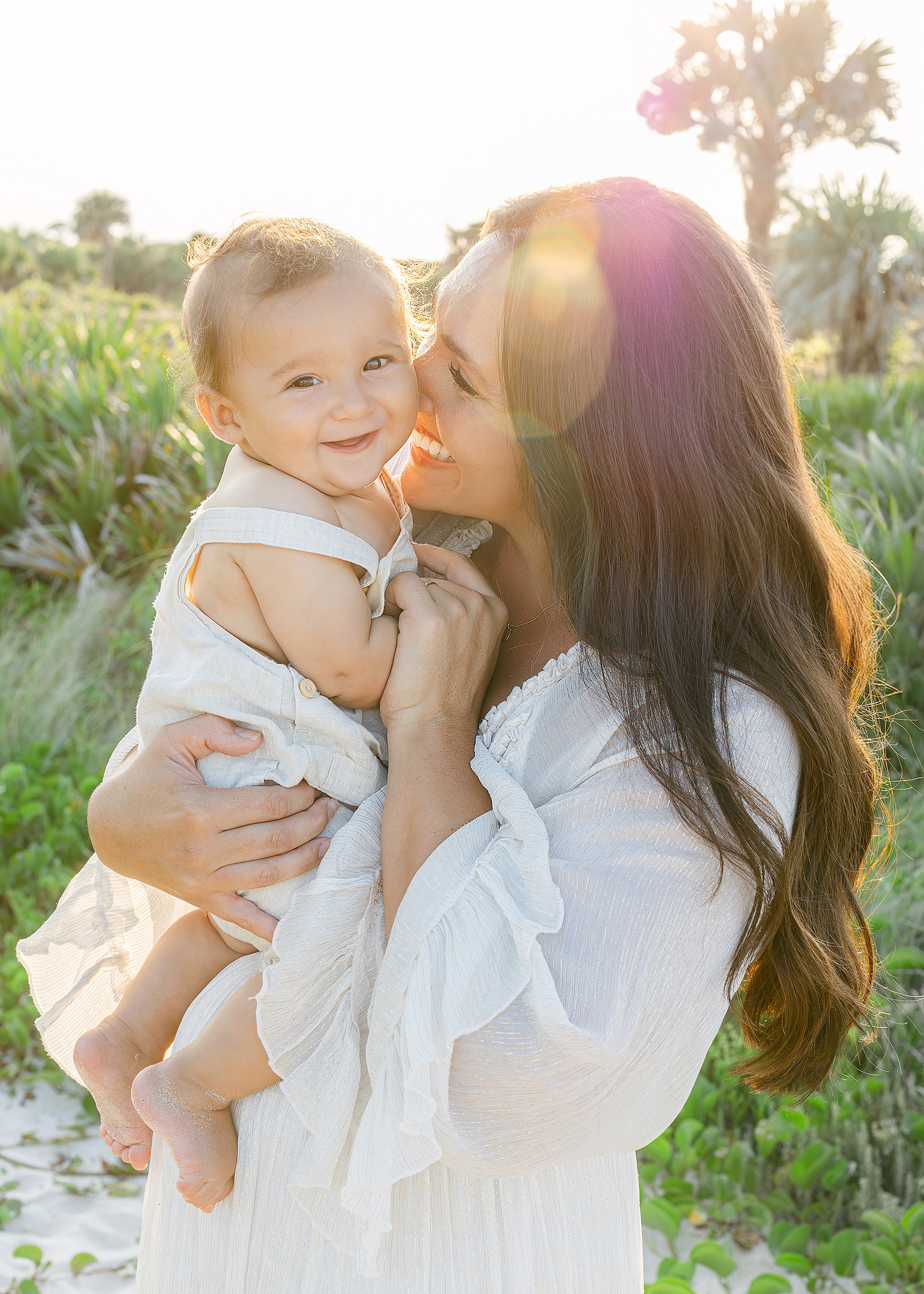 A sun filled backlit motherhood portrait of a woman with her baby boy on the beach.