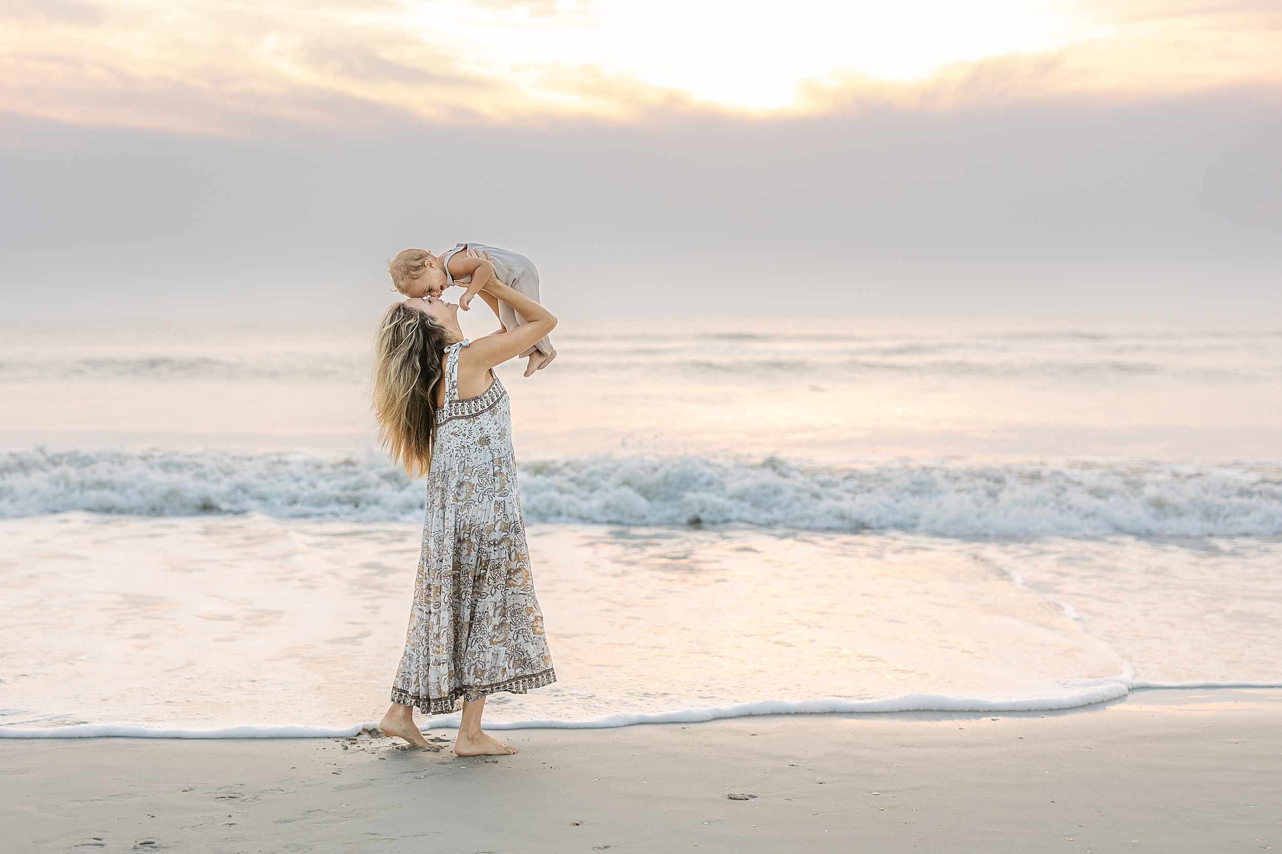 A mother holds her baby boy up in the air at sunrise in the surf on St. Augustine Beach, Florida.