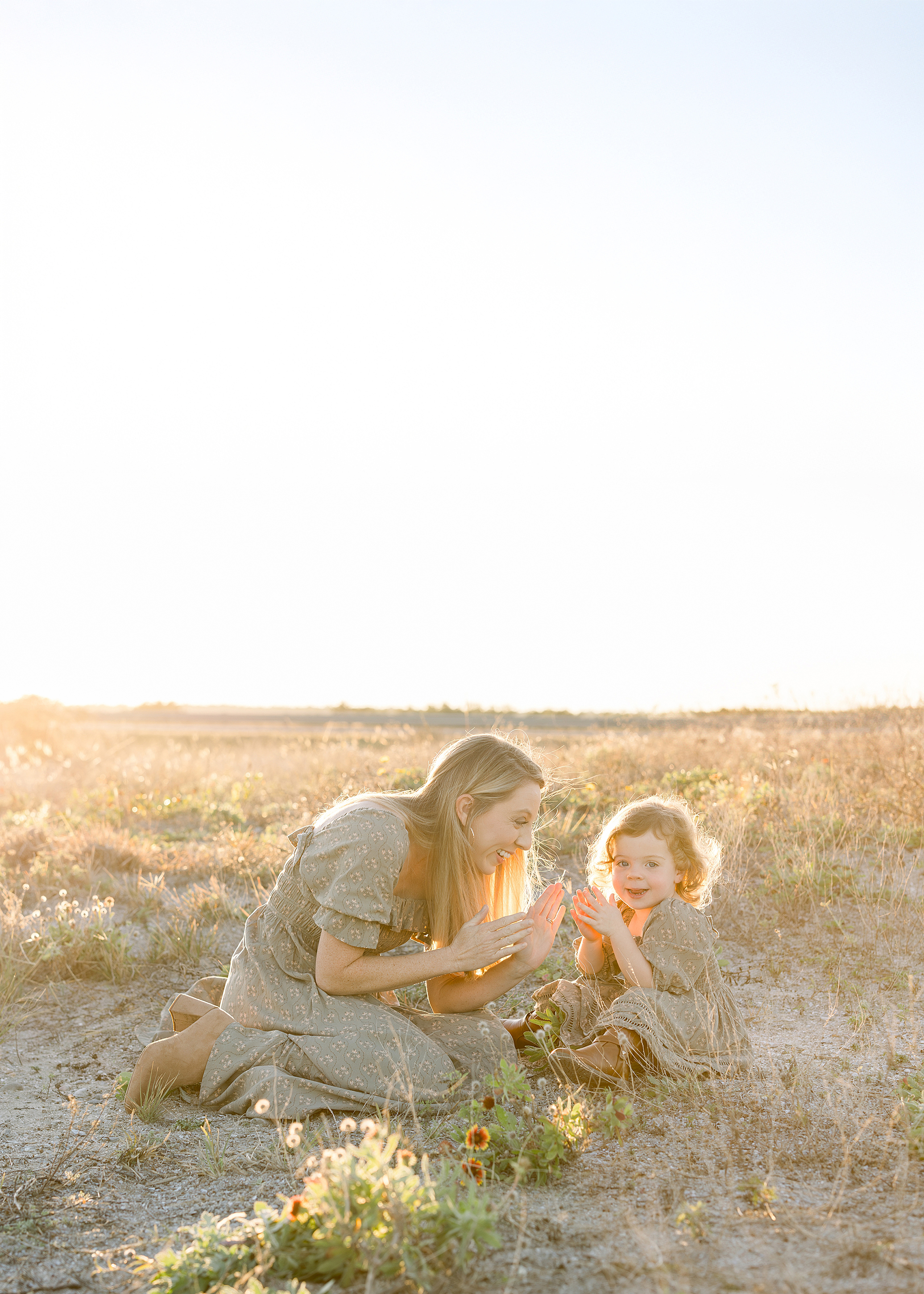 Mother plays with her toddler daughter in a flower field.