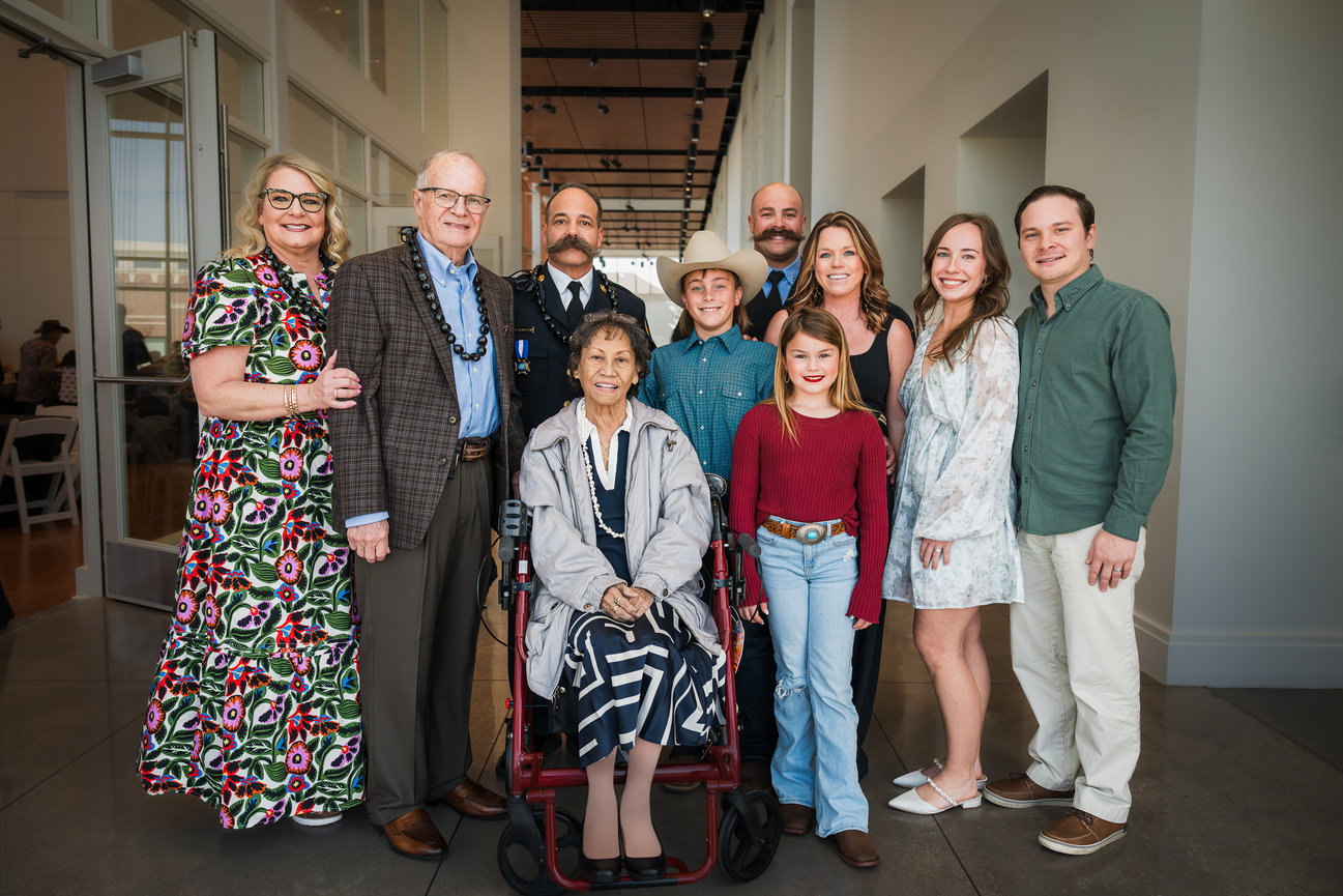 Multigenerational family posing indoors, including a woman in a wheelchair and a man in a cowboy hat.