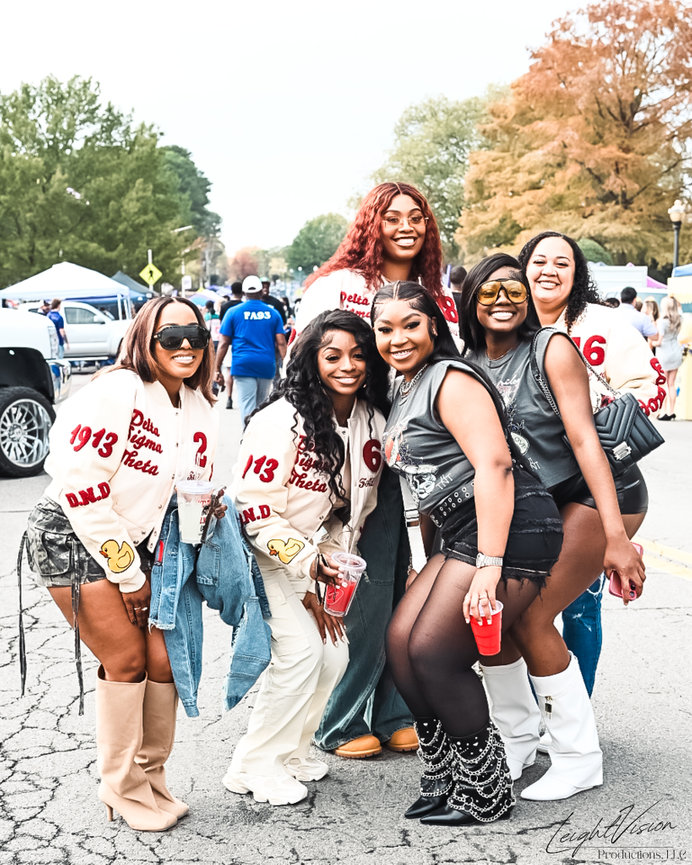 A group of women smiling and posing together for a photo at a lively football game.
