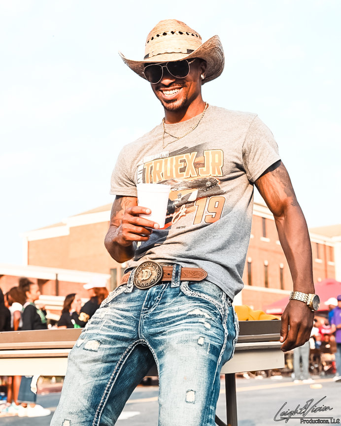 A man wearing a cowboy hat and jeans sits casually on a bench, enjoying a moment of relaxation outdoors.