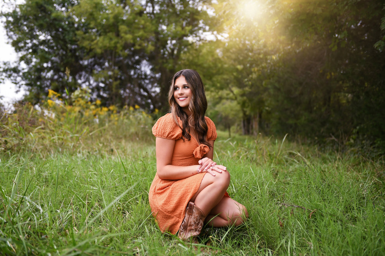 High school senior in orange dress grassy field at sunset during a high school senior session in Mocksville, NC, photographed by Megan Gioeli