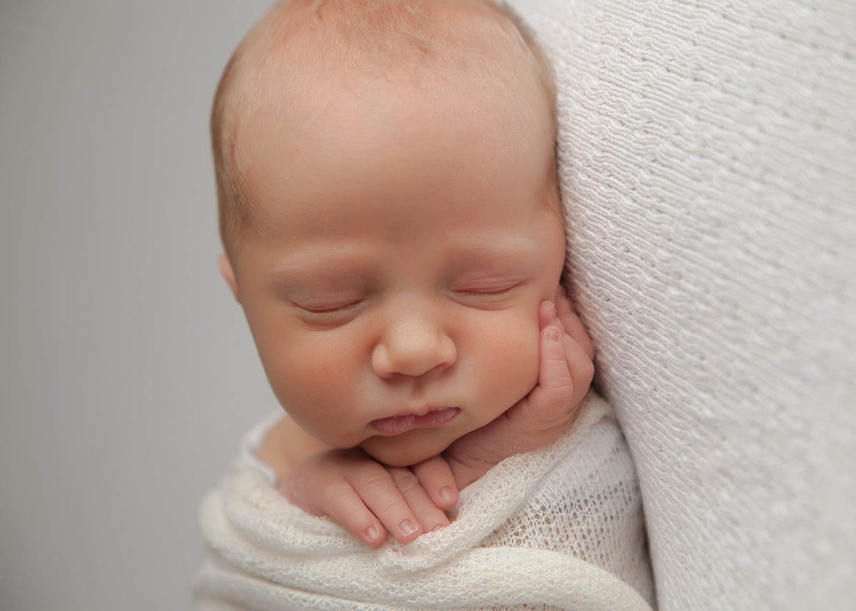 Close-up of a newborn hands resting on chin, captured in studio light with timeless fine art simplicity.