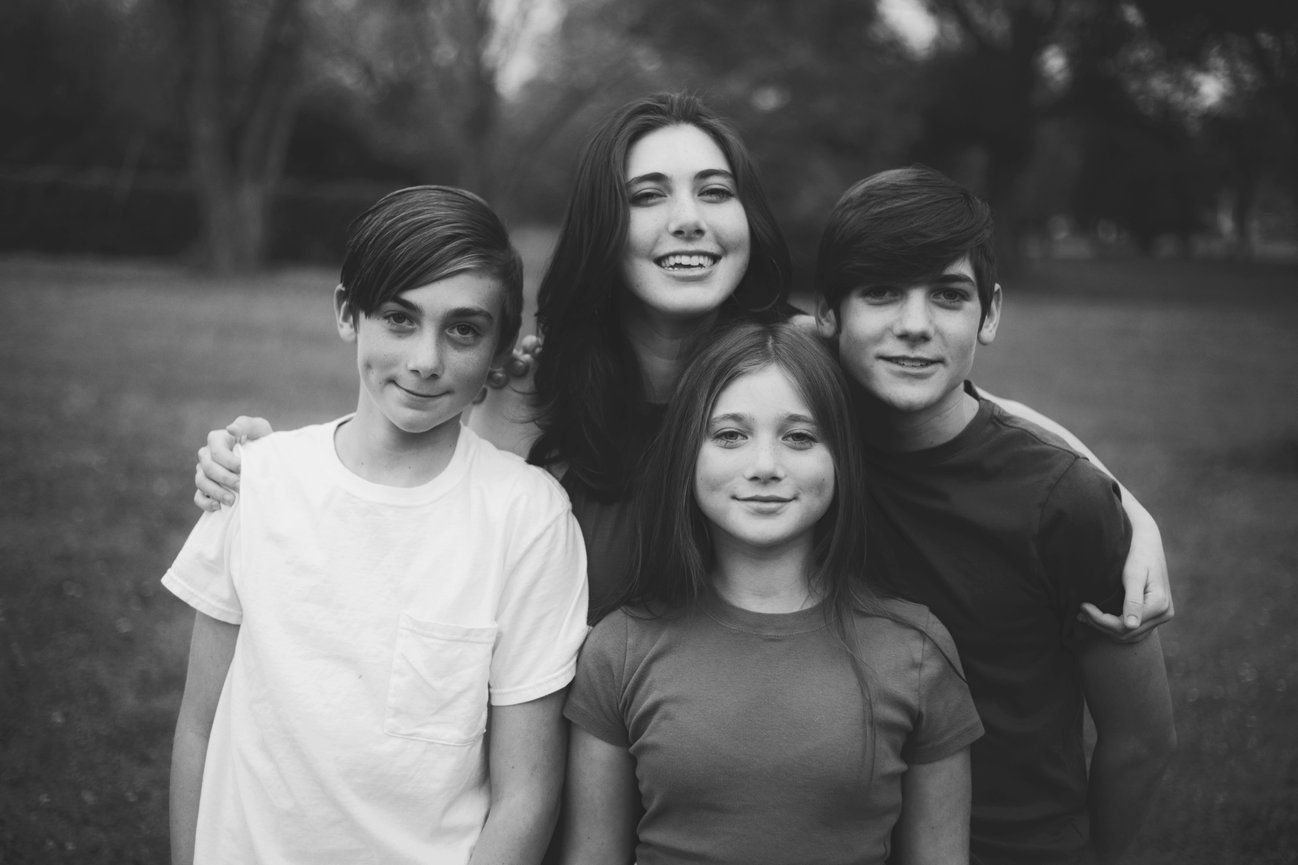 Black and white portrait of four siblings posing together outdoors.