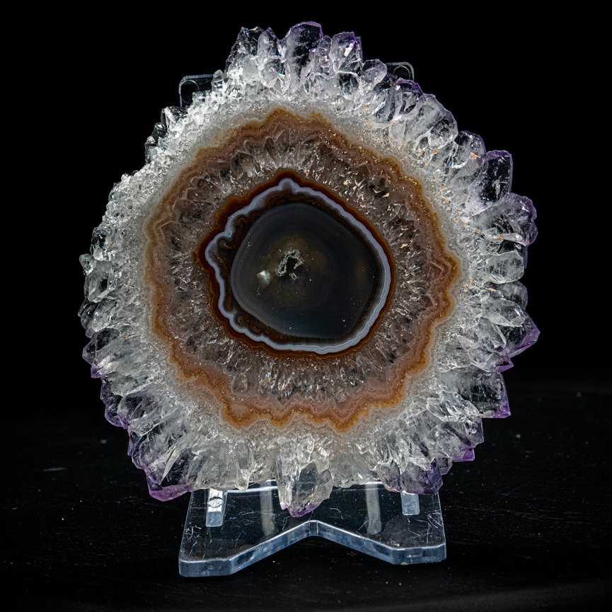 Crystal geode slice with purple quartz and dark agate center on a clear stand against a black background