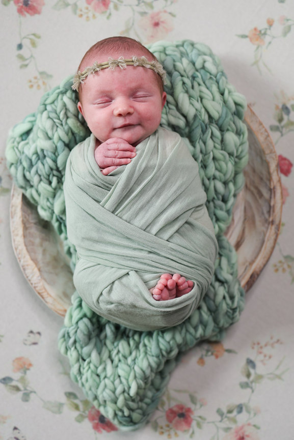 Newborn baby swaddled in mint green on a floral blanket