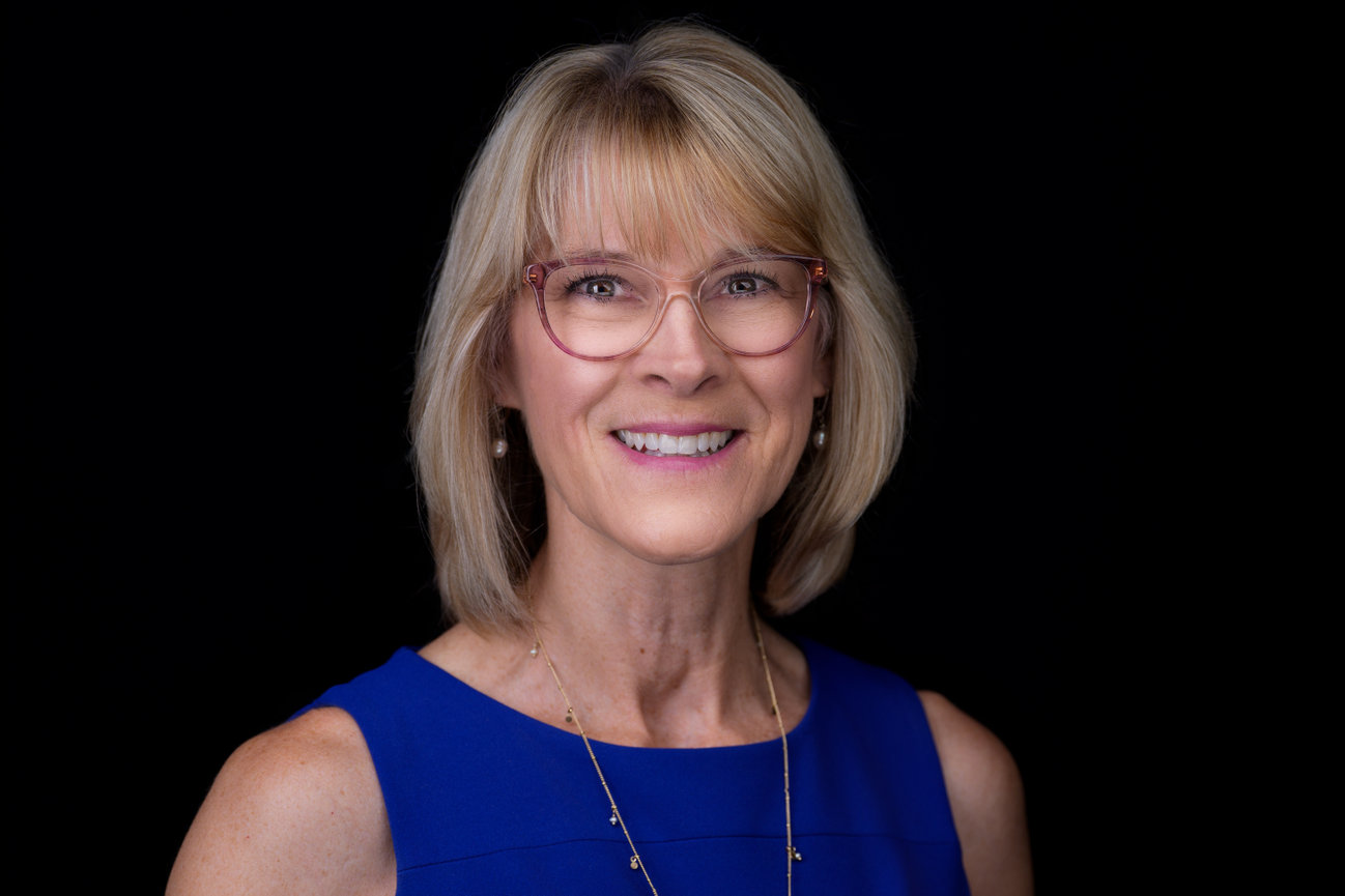 Professional studio headshot of woman with blonde hair and glasses wearing blue dress, taken in DFW portrait photography studio