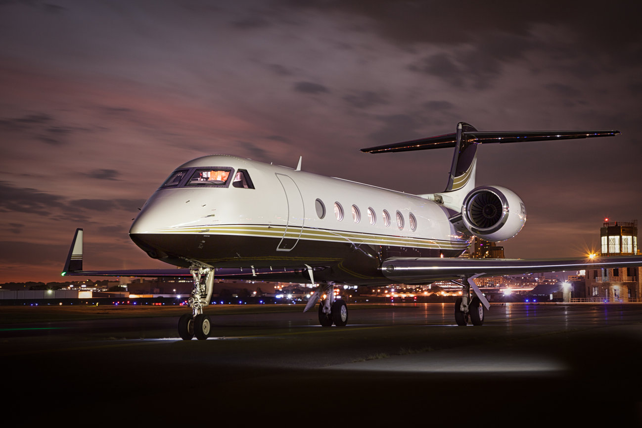Private jet on a runway at dusk with city lights in the background.