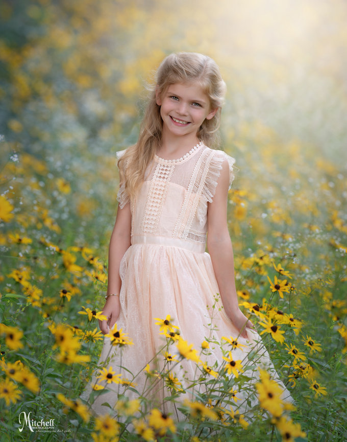 Smiling young girl in a pale pink dress standing in a field of yellow flowers
