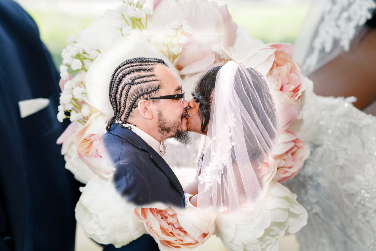 Bride and groom kissing during wedding ceremony with floral backdrop