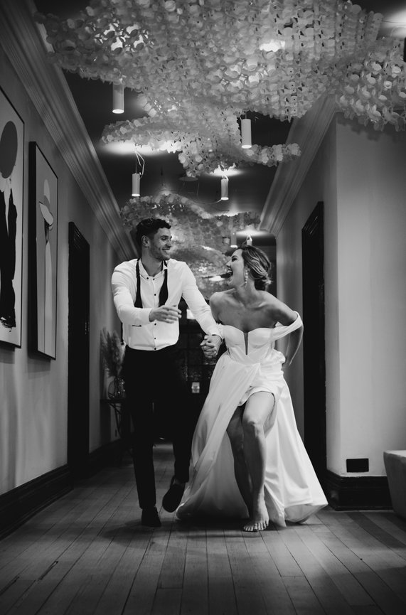 Editorial Wedding photography. A joyful couple in wedding attire runs down a decorated hallway at The Salt House, Standon Hall..
