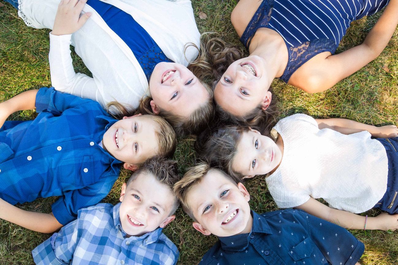 Smiling children lying in a circle on grass outdoors during family photo session in Blue Springs Missouri photographed by Case Studios Photography