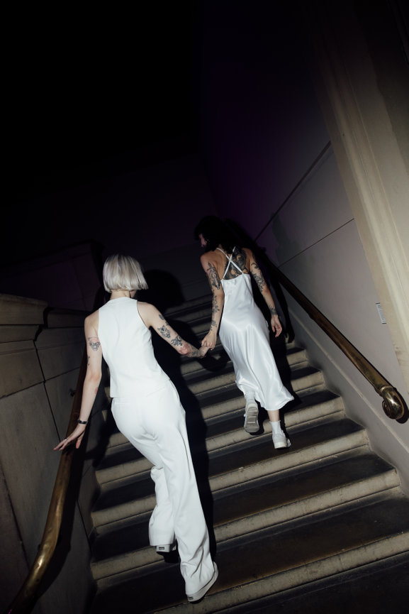 Direct flash photography as two brides in modern attire walk up the stone stairs at Manchester Art Gallery.