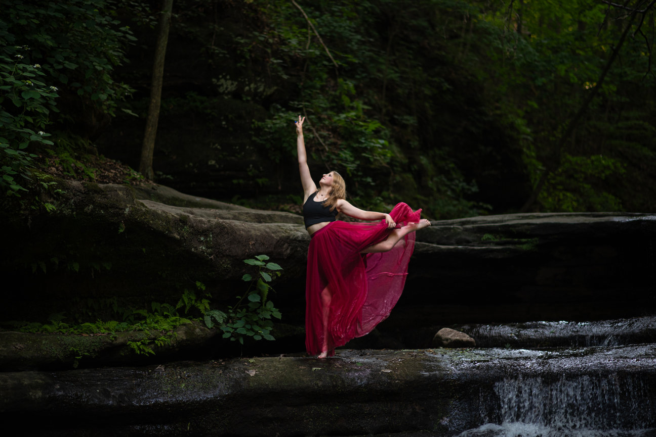 girl in red skirt dancing in a stream with waterfall