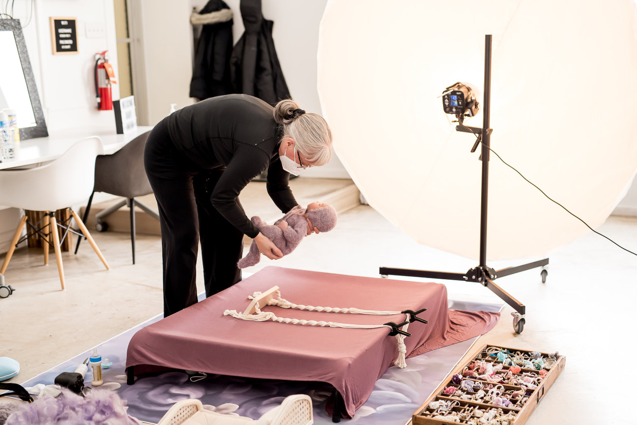 Person preparing a baby on a photography set with props and lighting equipment.