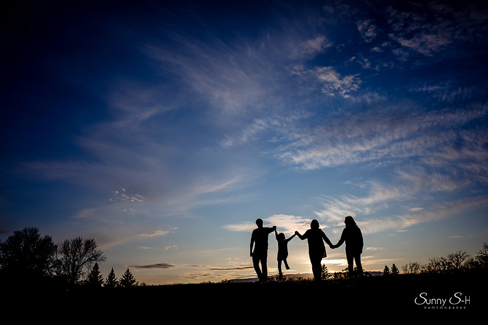 Silhouettes of four people holding hands against a vibrant sunset sky.