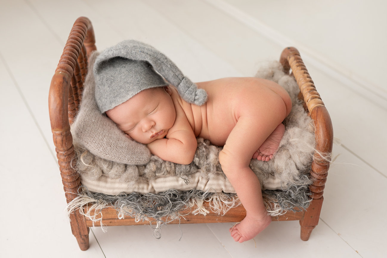 Neutral-toned newborn session with baby posed in a tiny bed prop