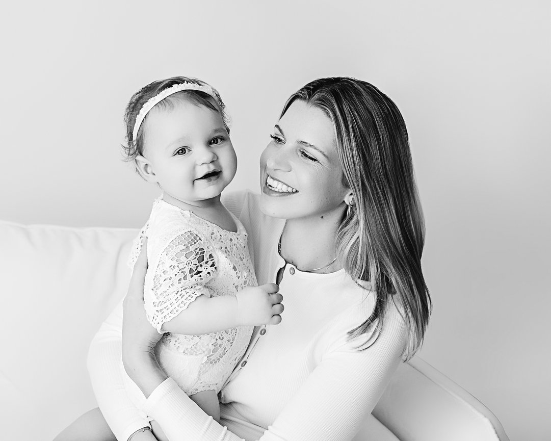 Mother kissing baby’s cheek on white background in Cranford