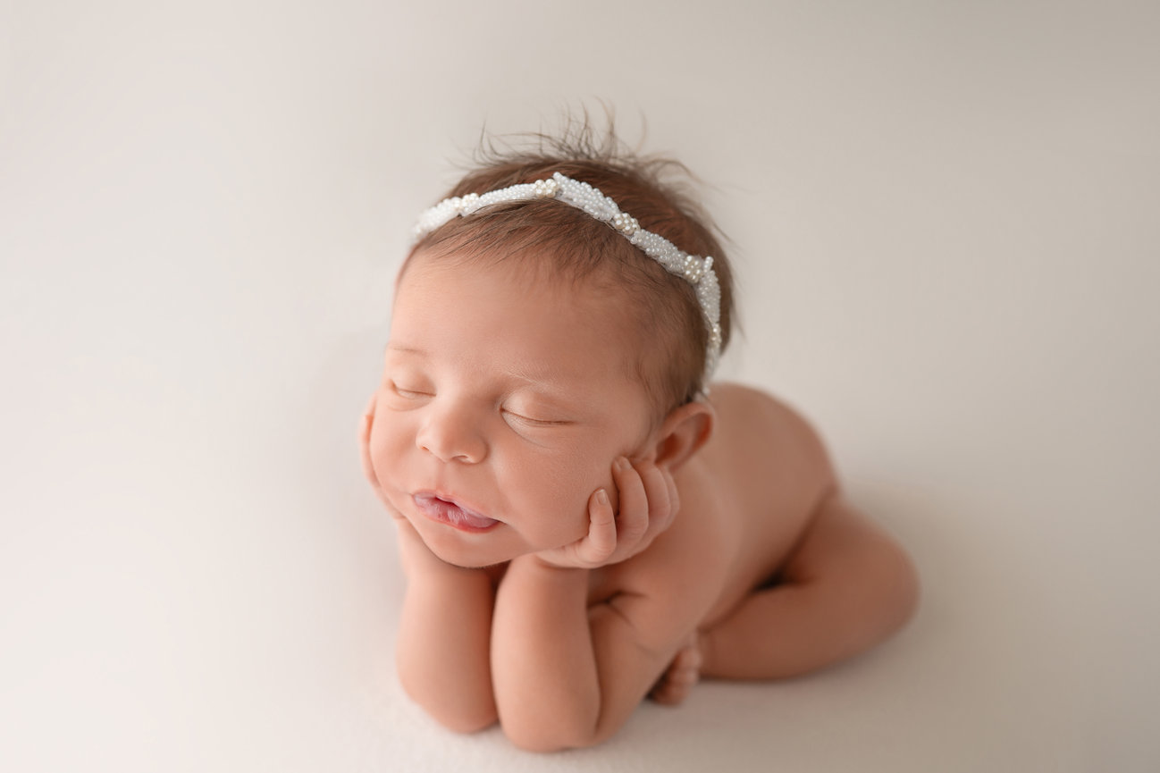 Newborn baby in froggy pose on solid neutral backdrop, showcasing flexibility and peaceful expression during studio session in Manasquan, NJ