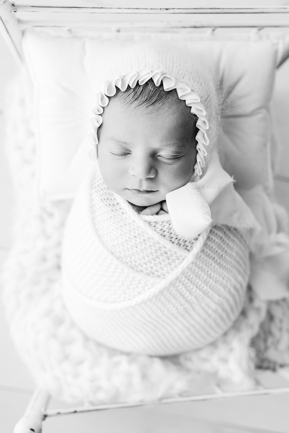 Warm and organic newborn setup: baby wrapped in chunky swaddle and posed in heirloom-style bed prop with cozy layers