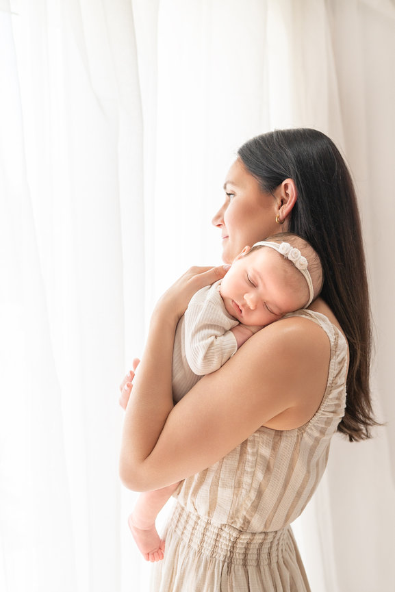 New mother standing in a naturally lit studio holding her young baby girl in a natural, candid position.