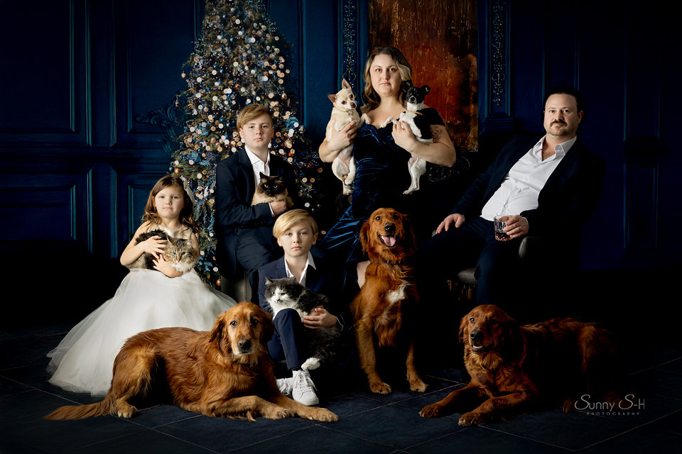 Family and dogs pose in front of a decorated Christmas tree in a festive setting.