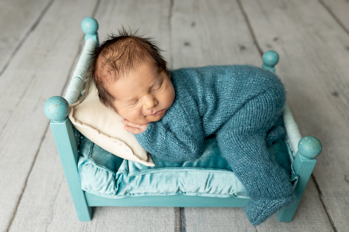 Baby boy in blue posed on a tiny bed during a studio newborn photography session in Winnipeg