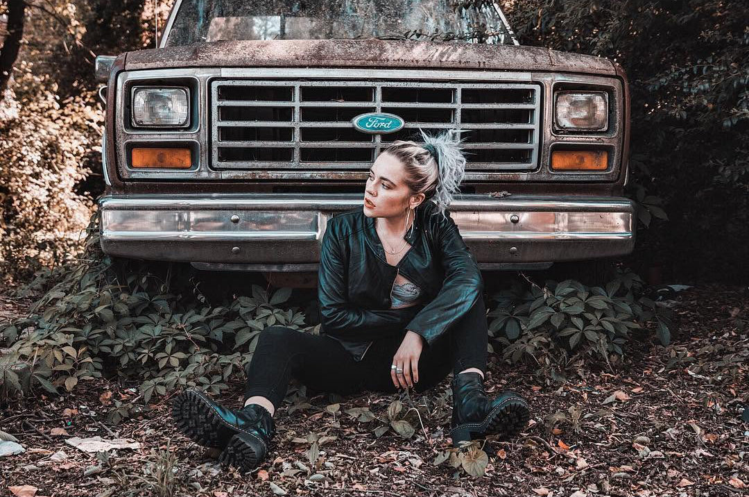 Woman sitting in front of an old truck in a wooded area