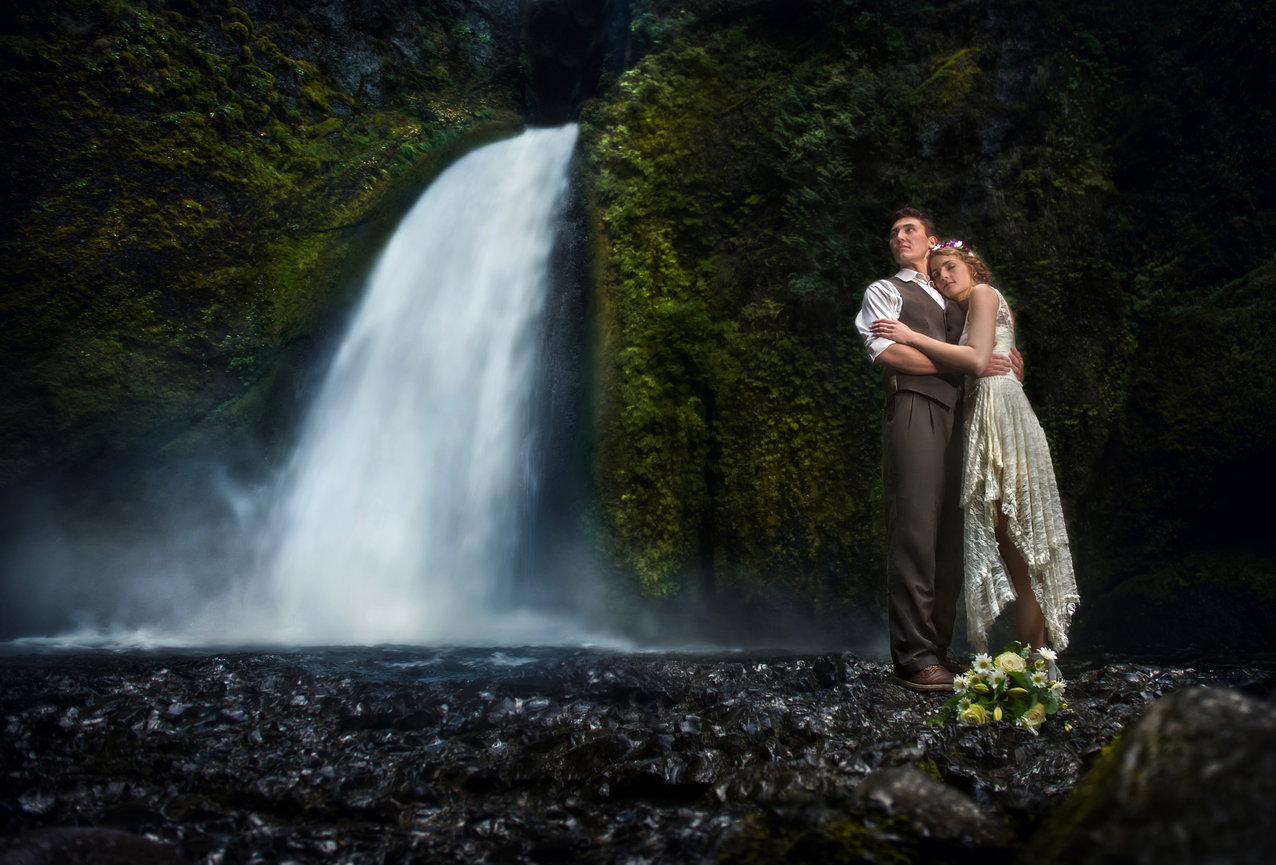 Couple embracing in front of a waterfall in a dark forest.