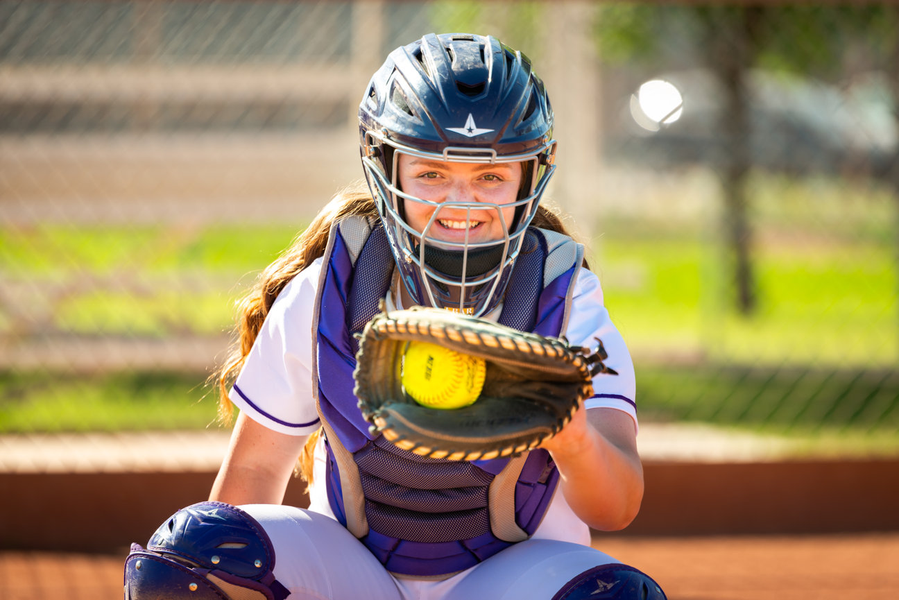 Senior girl in catcher’s gear crouching on softball field