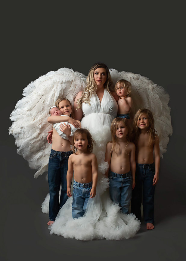 motherhood photo of mom wearing white angel wings while holding surrounded by her six children during newborn photoshoot with newborn photographer Dreamworks Photography in kansas city