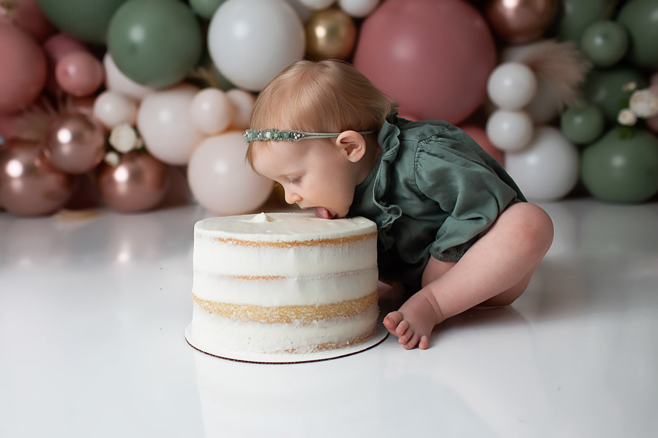 baby girl licking large white cake during first birthday cake smash photoshoot with Kansas City baby photographer dreamworksphotography