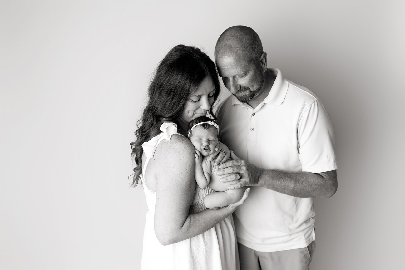 Omaha Baby Photographer captures couple lovingly holding their newborn baby wrapped in a blanket, with gentle smiles on their faces.