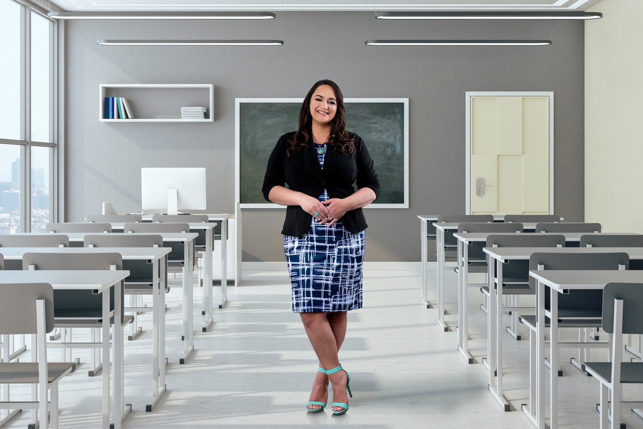 A woman instructor posing in the middle of a classroom smiling.