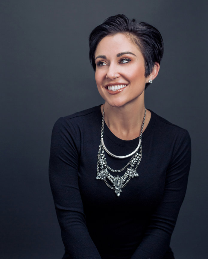 A beautiful fit brunette short haired woman in black with a large silver necklace looks to her right and smiles while posing for a professional model headshot in studio in Fishers Indiana.