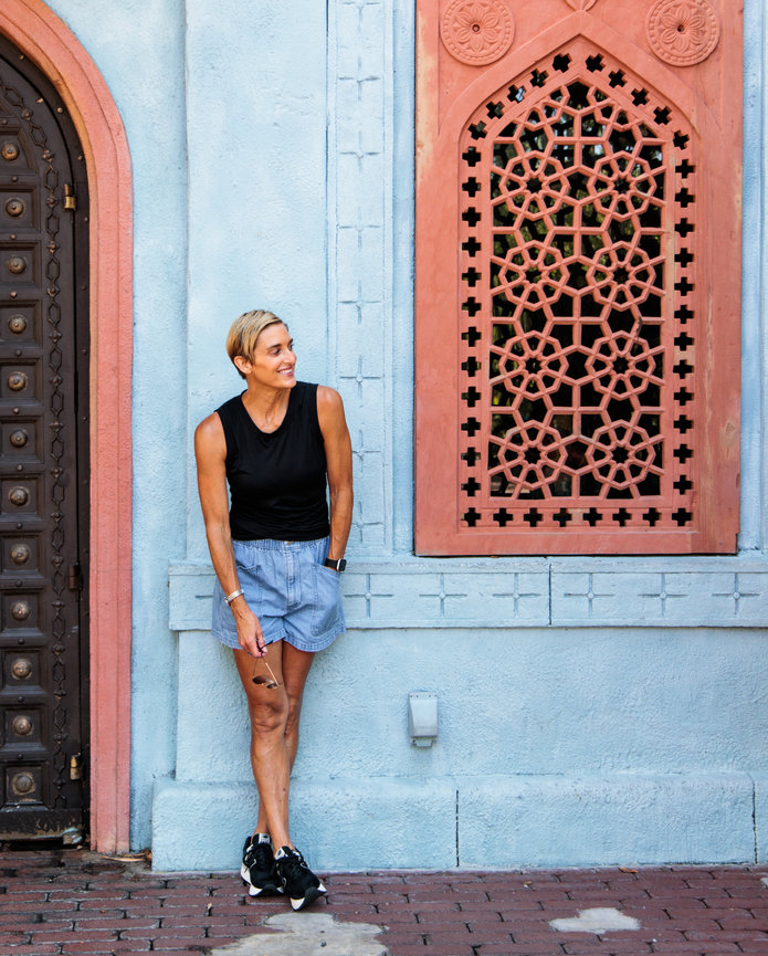 A beautiful fit woman with short blonde hair leans against a blue Moroccan inspired wall with red windows at Disney World in Orlando Florida.
