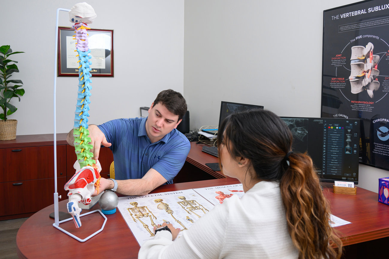 Chiropractor sitting at a desk across from a patient showing them a model spine.